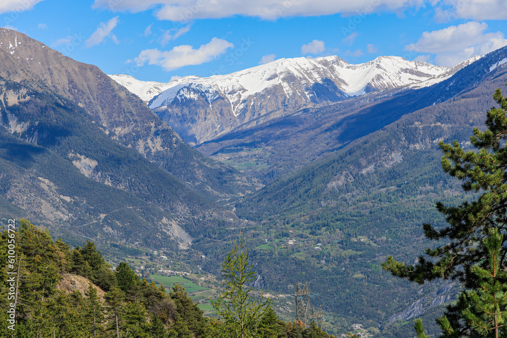 A scenic view of a mountain valley with a town surrounded by snowy mountain summit under a majestic blue sky