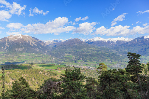 A scenic panoramic view of a mountain valley with a town surrounded by mountain summit under a majestic blue sky