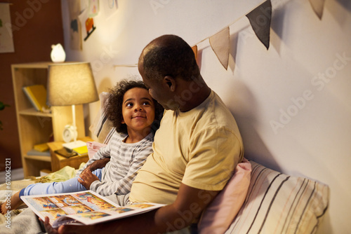 Canvas Print African American dad reading tale to his child before sleep, they watching pictu