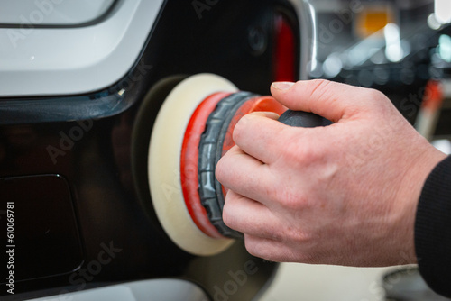 A car service worker polishes the car body with a polishing machine. Detailing and polishing of the car. Car detailing - hands with an orbital polishing machine in an auto repair shop.Selective focus. © Dmitry Presnyakov