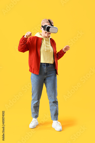 Young woman using VR glasses on yellow background © Pixel-Shot