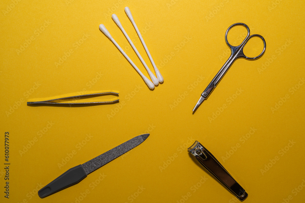 Fototapeta premium Cosmetic accessories with ear cleaners, scissors, nail clippers, nail file and tweezers on a yellow background