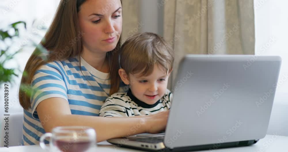 Mother working on laptop from home remotely with little son in her arms. Mother working on laptop from home remotely with little son in her arms.