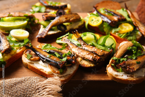 Board of tasty sandwiches with canned smoked sprats on wooden background photo