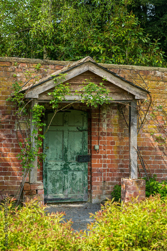 Painted green door and wooden porch as entrance to walled garden made with brick
