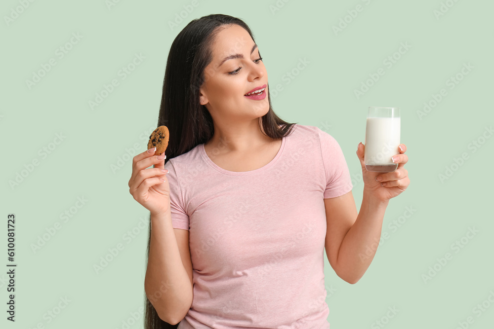 Beautiful young woman with glass of milk and cookie on mint background Beautiful young woman with glass of milk and cookie on mint background