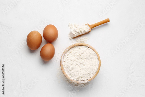 Wooden bowl with wheat flour, scoop and eggs on white background