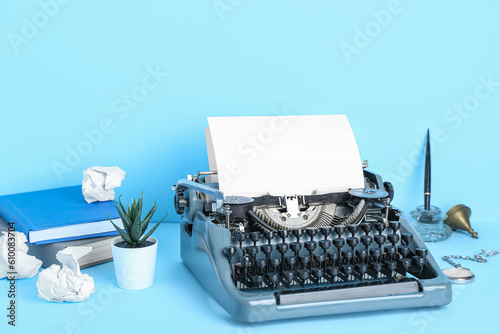 Vintage typewriter with books, pocket watch and pen holder on blue background