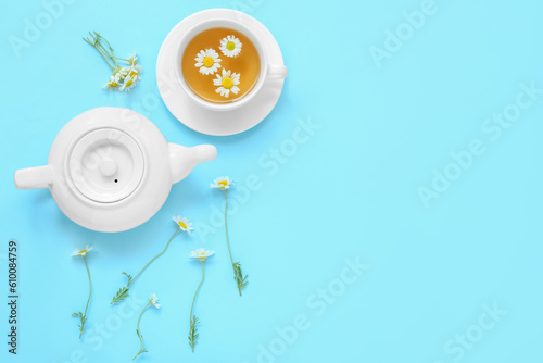 Teapot with cup of hot chamomile tea on blue background