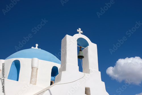A cross with bells on the top of an orthodox whitewashed church in Ios Greece and a blue sky in the background in Ios Greece