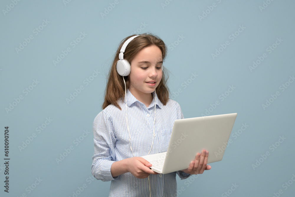 Portrait of a young girl with a small white laptop and white headphones. pastel aquamarine background Portrait of a young girl with a small white laptop and white headphones. pastel aquamarine background