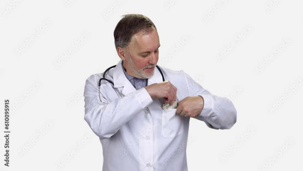 Male senior aged doctor with stethoscope puts his money in a coat pocket. Isolated on white. Male senior aged doctor with stethoscope puts his money in a coat pocket. Isolated on white.