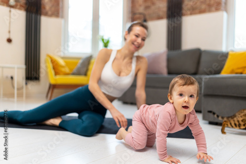 Young sporty mother and baby girl working out exercising together at home.