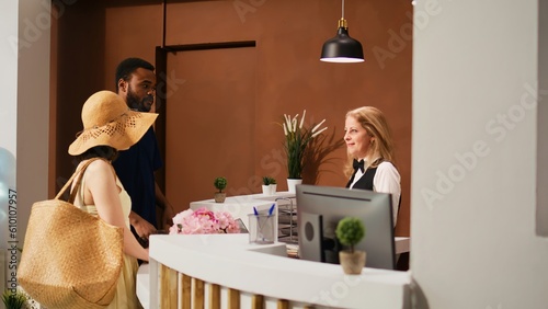 Hotel staff welcoming guests at front desk, preparing to register on booking reservation. People arriving at tropical resort, talking to employee at reception about accommodation.