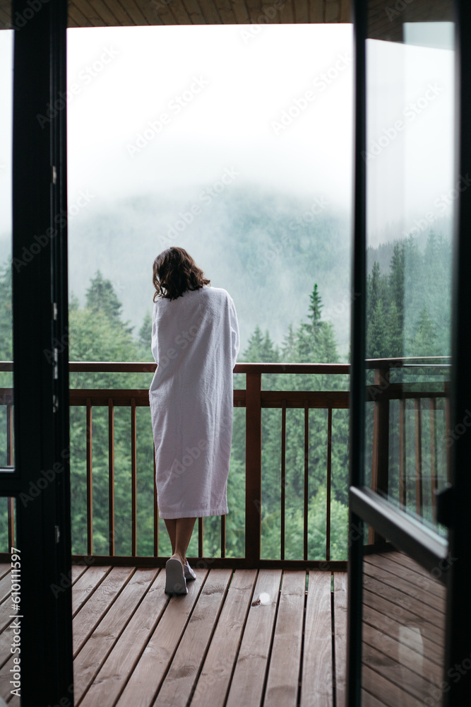 A young woman stands on the balcony of a room overlooking the mountains A young woman stands on the balcony of a room overlooking the mountains
