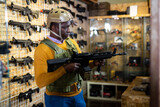African-american man wearing military vest and holding machine gun in air weapon shop.