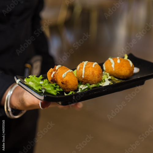 typical Spanish croquettes dipped in sauce, held by the hands of a waitress