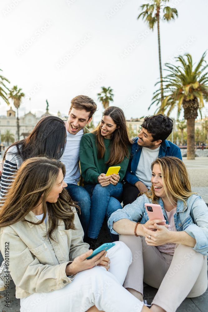 Fototapeta premium Multiracial group of young friends with mobile phone enjoying a day off social meeting outdoors. Millennial generation people relaxing together outdoors while talking and laughing. Youth community