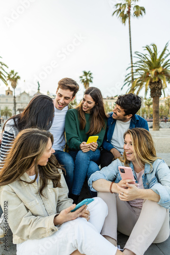 Multiracial group of young friends with mobile phone enjoying a day off social meeting outdoors. Millennial generation people relaxing together outdoors while talking and laughing. Youth community