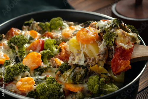 Gratin with broccoli, carrots and cheese baked in the oven on a dark wooden table