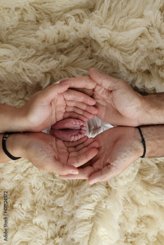 Feet of the newborn on the palms of the parents. The palms of the father and mother are holding the foot of the newborn baby in a white flokati blanket. Photography of a child's toes, heels and feet.