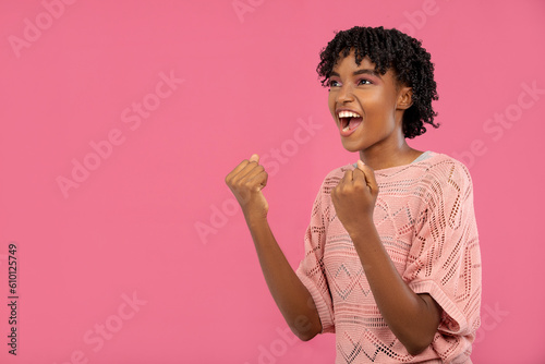 young brunette woman raised her hands and is screaming looking up. beautiful woman is joyfully shouting in victory on a pink background, with text space 