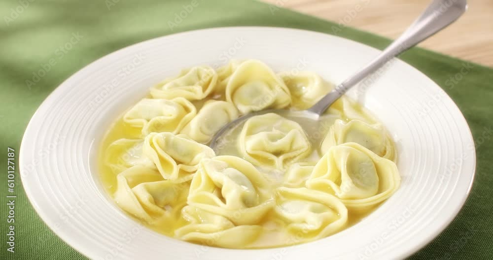 pasta tortelloni with ricotta and spinach in chicken broth with spoon. hot italian pasta on a white plate. ready to eat food. green background. sunny day. angle view. smooth slide camera movement. pasta tortelloni with ricotta and spinach in chicken broth with spoon. hot italian pasta on a white plate. ready to eat food. green background. sunny day. angle view. smooth slide camera movement.