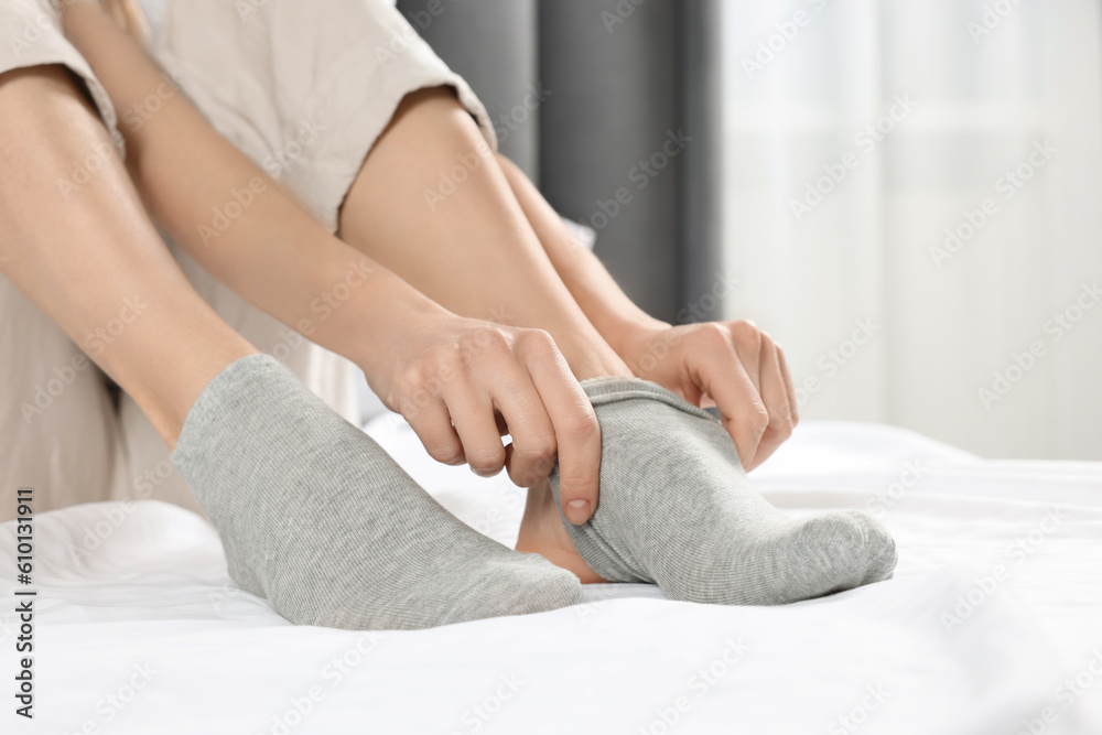 Obraz premium Woman putting on grey socks in bedroom, closeup