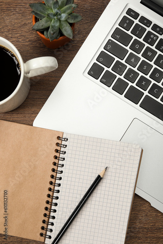 Modern laptop, notebook, pencil, cup of coffee and houseplant on wooden table, flat lay
