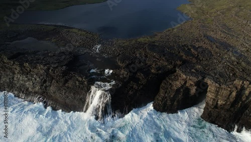 impressive aerial shot over the beautiful waterfall which is located in the lake SØRVÁGSVATN in the Faroe Islands and during sunset. You can appreciate the force of the waves breaking. photo