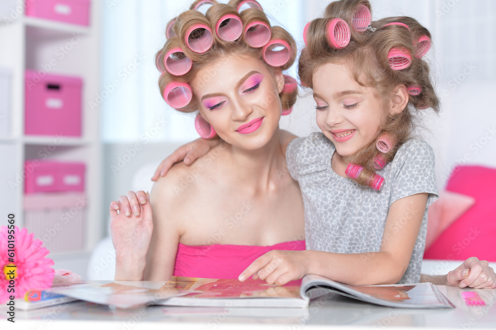 Mom and daughter with hair curlers reading magazine Mom and daughter with hair curlers reading magazine