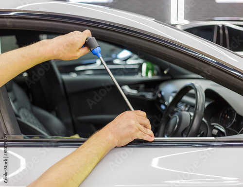 A specialist repairs a dent on the car body without painting. PDR. Process of paintless dent repair on car body. The mechanic at the auto shop with tools to repair dents in car body. Body repair.