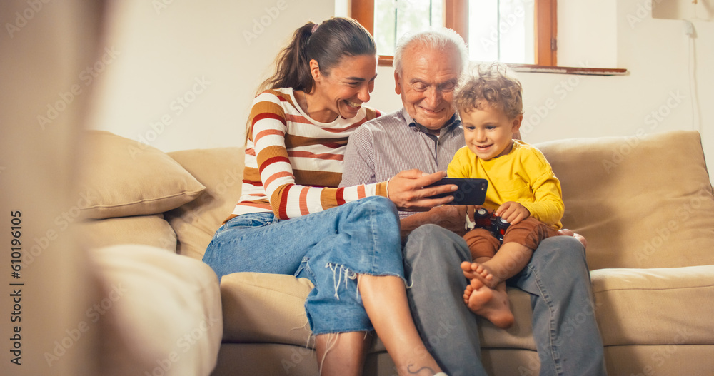 Happy Small Family Gathered Together, Sitting on a Sofa in the Living Room and Using a Smartphone. Mother, Son and Grandfather Watching Videos on a Mobile Phone and Laughing. They are Bonding Happy Small Family Gathered Together, Sitting on a Sofa in the Living Room and Using a Smartphone. Mother, Son and Grandfather Watching Videos on a Mobile Phone and Laughing. They are Bonding