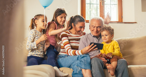 Happy Small Family Having Video Call on Smartphone While Sitting on Sofa in the Living Room. Family of 3 Generations Connecting to a Distant Relative Through Internet, Staying in Touch with Technology