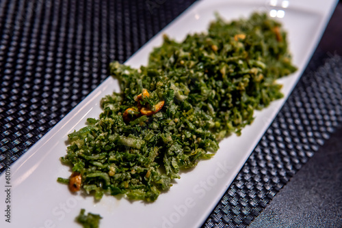 Close-up shot of a plate of crackling spinach, perfectly semi-fried to a crispy texture. It has a vibrant green color and mouth watering presentation. In terms of its health benefits, it is considere