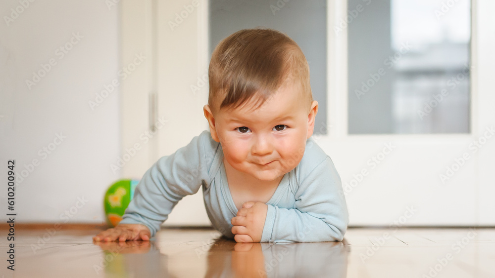 Portrait of cute happy smiling baby boy crawls on the home floor and looking at camera. Joy and happiness concept. Front view. Love and family emotion Portrait of cute happy smiling baby boy crawls on the home floor and looking at camera. Joy and happiness concept. Front view. Love and family emotion