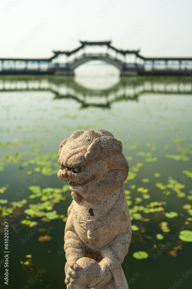 Chinese traditional style stone lion with wooden bridge and lotus pool in background