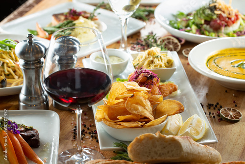 A view of a table full of a variety of entrees, featuring potato chips, red wine, soup, and salad.