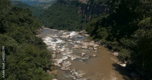 A drone aerial along river rapids flowing through wooded forest to a dramatic view of Karkloof Falls cascading over the edge of a sheer cliff to the view directly below. photo