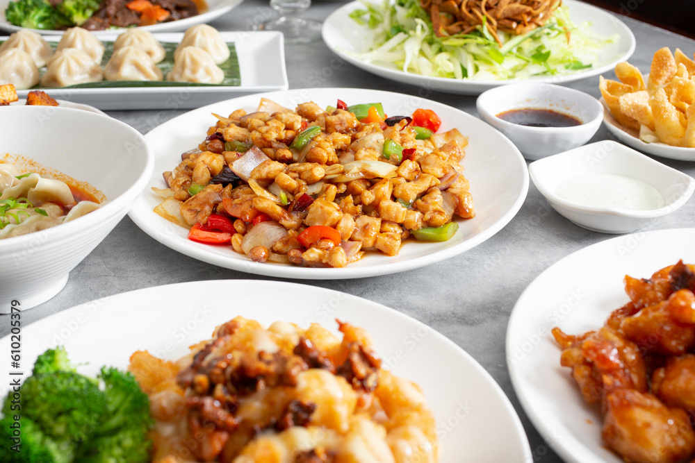 A view of a table full of various Chinese entrees, featuring kung pao chicken.