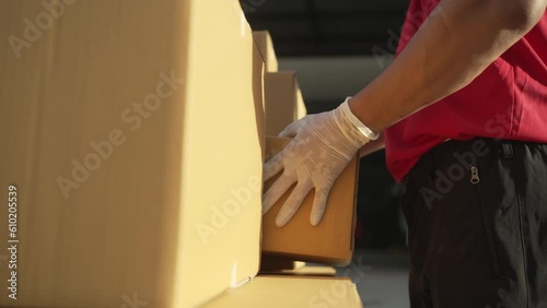 A parcel delivery worker dressed in a red uniform is lifting a package from the trunk of the truck to the recipient. contact the receiver in front of the house.