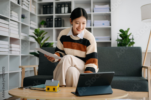 Young real estate agent worker working with laptop and tablet at table in home office and small house beside it.