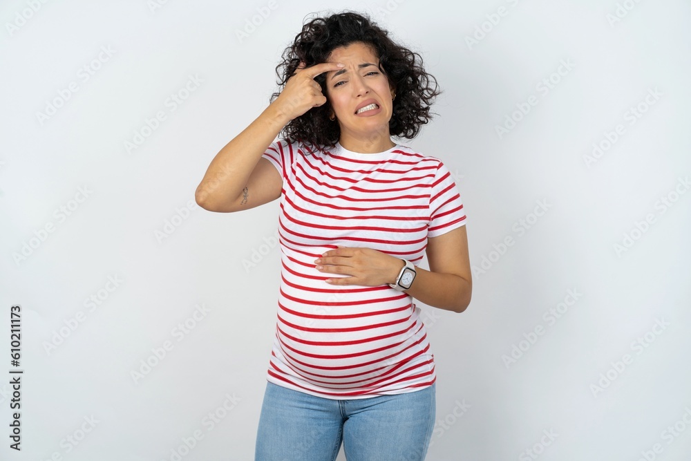 young pregnant woman wearing striped t-shirt over white background pointing unhappy at pimple on forehead, blackhead infection. Skincare concept. young pregnant woman wearing striped t-shirt over white background pointing unhappy at pimple on forehead, blackhead infection. Skincare concept.