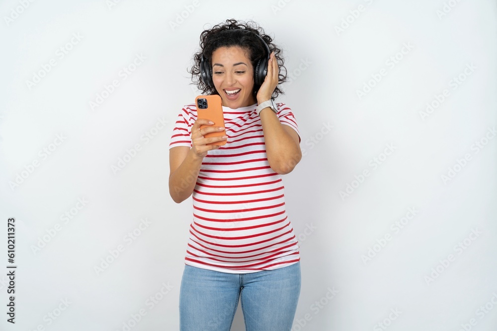 Happy young pregnant woman wearing striped t-shirt over white background feels good while focused in screen of smartphone. People, technology, lifestyle Happy young pregnant woman wearing striped t-shirt over white background feels good while focused in screen of smartphone. People, technology, lifestyle