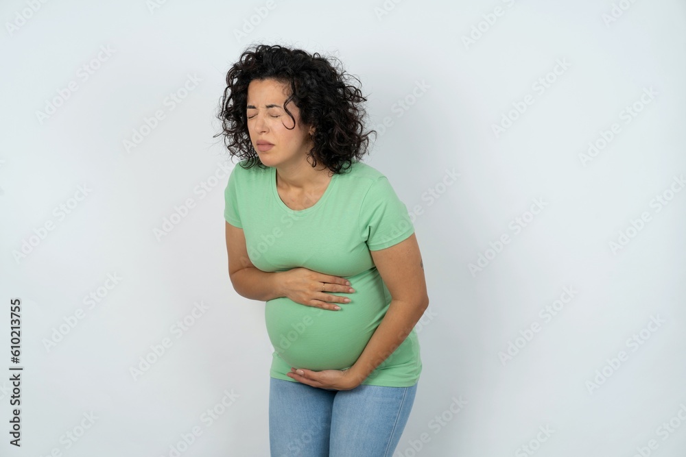young pregnant woman wearing green t-shirt over white background got stomachache