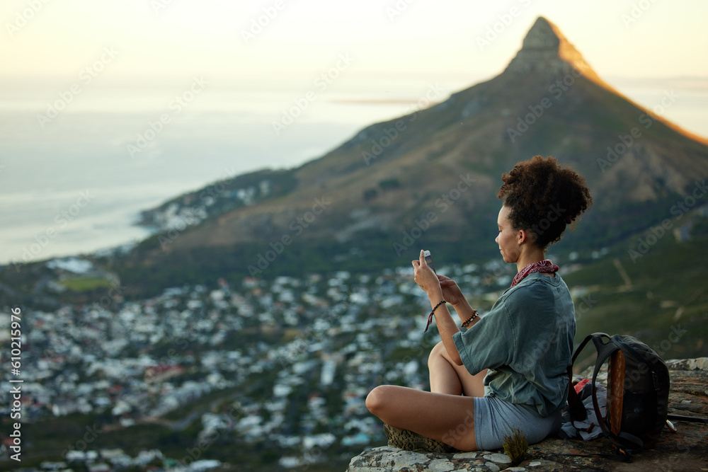 Obraz premium Woman, hiking and phone on mountain for travel in cape town for wellness on the weekend. Female hiker, mobile and adventure on a cliff with cityscape for scenery of lions head in the outdoor.