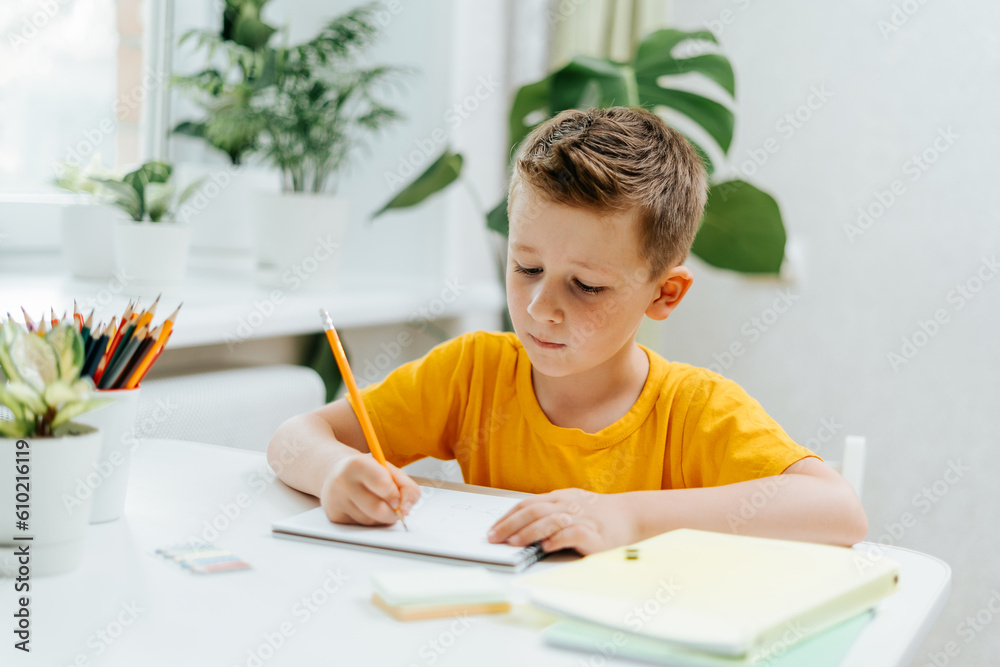 School kid boy studying at home with book, draw in notepad and doing homework. Thinking caucasian child siting at table with notebook. Back to school. Distance learning online education. School kid boy studying at home with book, draw in notepad and doing homework. Thinking caucasian child siting at table with notebook. Back to school. Distance learning online education.