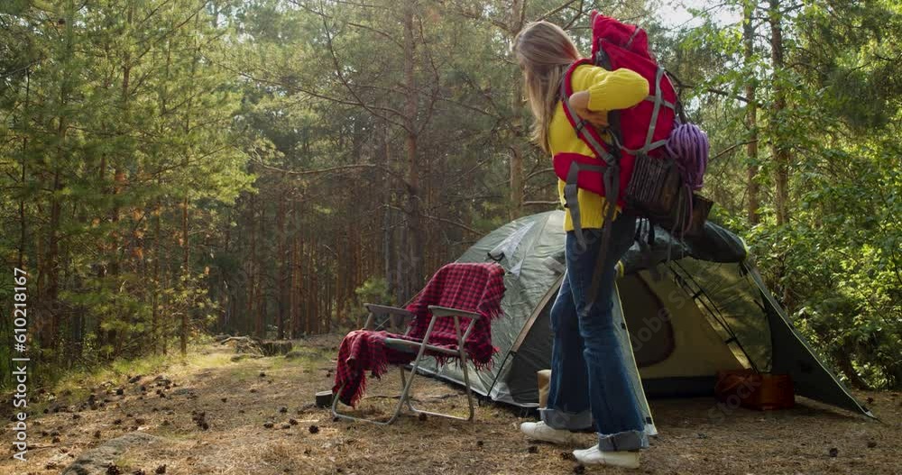 Zoom-in of a young woman near a tent in a pine forest. Take off your backpack and relax. Solitude with your thoughts and nature. Nature as a path to mental health. Zoom-in of a young woman near a tent in a pine forest. Take off your backpack and relax. Solitude with your thoughts and nature. Nature as a path to mental health.