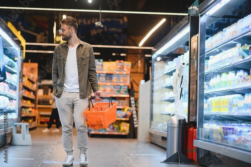 Young man buying groceries at the supermarket. Other customers in background. Consumerism concept.