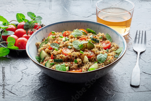 Quinoa tabbouleh salad in a bowl, a healthy dinner with tomatoes and mint, on a black slate background